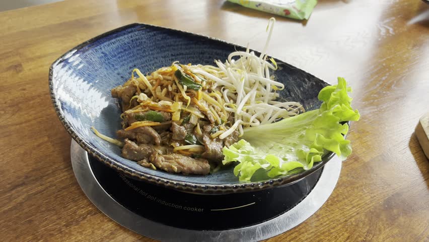 Nuts are falling on Pad thai or phad tha asian noodles closeup. Chinese rice pasta, phat thai with meat, noodles, fresh cabbage salad and greens in street restaurant on blurred background