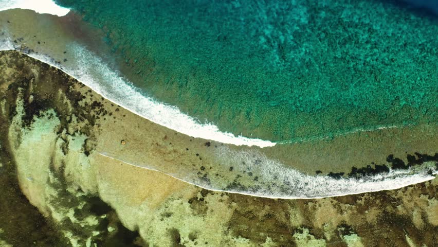 Aerial view of turquoise water meeting land with waves crashing, creating a striking contrast between the ocean and the shore, Maldives.