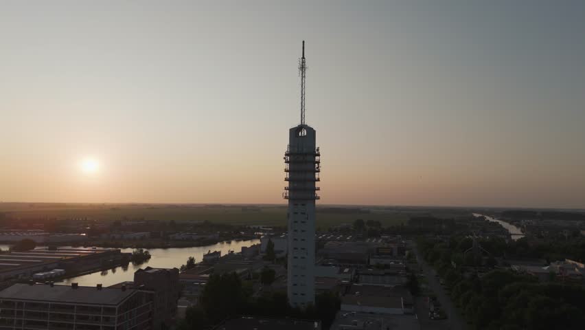 Scenic drone footage of a tall communication tower during golden hour, overlooking a winding river, bridges, and an urban skyline in The Netherlands