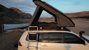 Drone fly-through over rooftop tent campsite beside a calm river, framed by majestic mountains. Perfect for camping, outdoor adventure, travel, and nature projects. - Powered by Shutterstock - Get 15% off with code: PIKWIZARD15