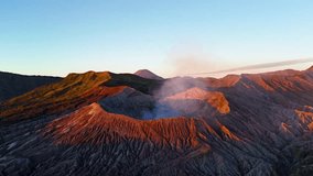 Forward moving drone hyperlapse at sunrise sweeps across the Tengger caldera, passing the smoking rim of Mount Bromo toward distant Semeru, which erupts in an ash plume finale. - Powered by Shutterstock - Get 15% off with code: PIKWIZARD15