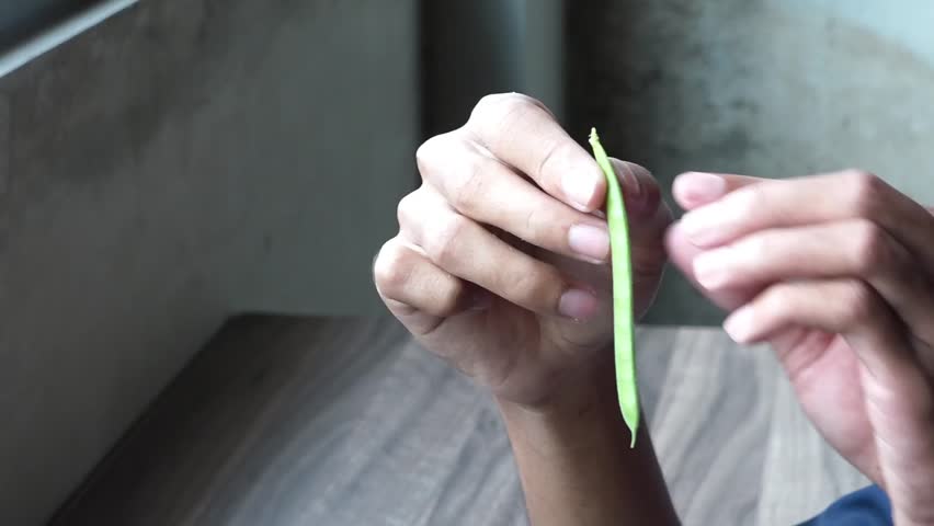 Hands peeling fresh green long bean pod on wooden table.
