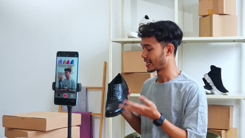 Young Man Presenting Shoes To Smartphone Camera For Online Product Review Or Sale