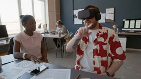 Young adult male UX designer wearing VR headset simulating user testing while discussing optimization ideas with African American female colleague working collaboratively at office desk - Powered by Shutterstock - Get 15% off with code: PIKWIZARD15