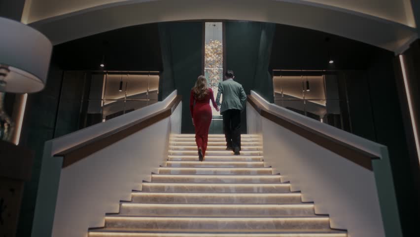 Guy and a girl in beautiful clothes are walking up the steps in the lobby of an expensive restaurant to the second floor