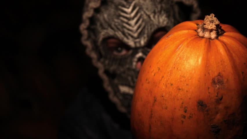 Scary Halloween Scene. Masked Monster with a Skull Carrying a Pumpkin at Night. Surreal Halloween.
