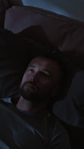 Vertical close-up time lapse of face of man lying in bed at night with open eyes suffering from insomnia, staring in darkness, doing breathing exercise to fall asleep, shadows from car lights on walls