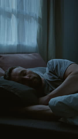 Vertical time lapse of young Caucasian man suffering from PTSD turning and squirming in bed at night, experiencing violent nightmare, suffering from sleep deprivation