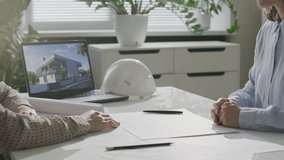 Two female architects shaking hands over desk with architectural plans and laptop, then discussing project during meeting in sunlit office. Close-up view - Powered by Shutterstock - Get 15% off with code: PIKWIZARD15