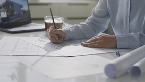 Close up view of female architect sketching building floor plan on paper while sitting at office desk with laptop and cup of coffee nearby - Powered by Shutterstock - Get 15% off with code: PIKWIZARD15