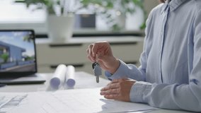 Hand of female real estate agent giving house shaped keychain with keys to customer above office desk with blueprints, coffee cup and laptop. Close-up view - Powered by Shutterstock - Get 15% off with code: PIKWIZARD15
