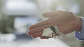 Close up view of hand of unrecognizable woman holding house keys with silver home shaped keychain in open palm in sunlit office, symbolizing property ownership or rental - Powered by Shutterstock - Get 15% off with code: PIKWIZARD15