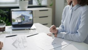 Female real estate agent handing house keys to client over table with architectural drawings and laptop displaying modern home during meeting in sunlit office. Close-up shot - Powered by Shutterstock - Get 15% off with code: PIKWIZARD15