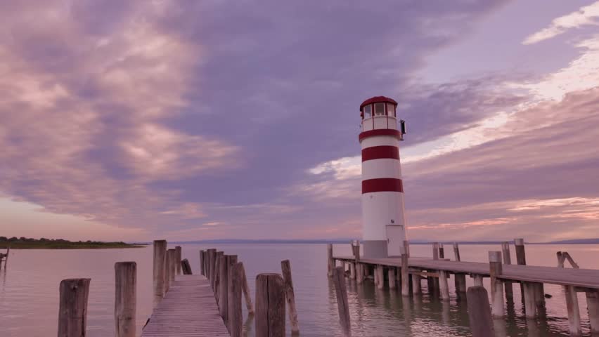Podersdorf Lighthouse with piers on Neusiedler See, Austria, under a soft purple-pink sunset. Calm lake and pastel sky create serene, idyllic atmosphere.
