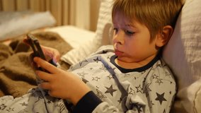 Cute kid boy in pajamas lying in bed watching smartphone, smiling. Children's screen time. Child plays games using phone at the evening or night. Social media addiction. Childhood, modern technology
 - Powered by Shutterstock - Get 15% off with code: PIKWIZARD15