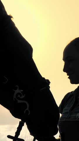Horse riding. Horse love. Silhouettes of a young woman and her horse, at sunset, on sky background and sun rays backlight. friendship between man and horse. Equitation.