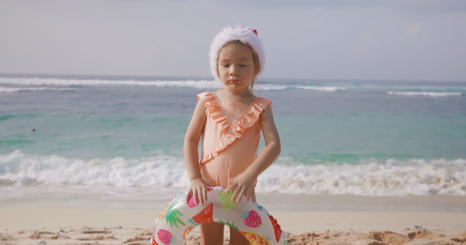 Little child girl staying on ocean beach with Christmas hat. Winter vacation in Bali