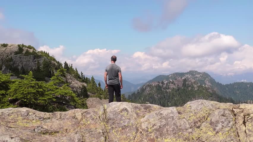 Man Stands Atop a Mountain Peak, Gazing at the Vast Wilderness of British Columbia, Canada.