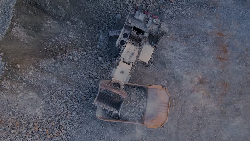 Aerial view of gold ore extraction and hauling in an open pit mine, mining industry. Process excavator loads rocks into big dump truck.