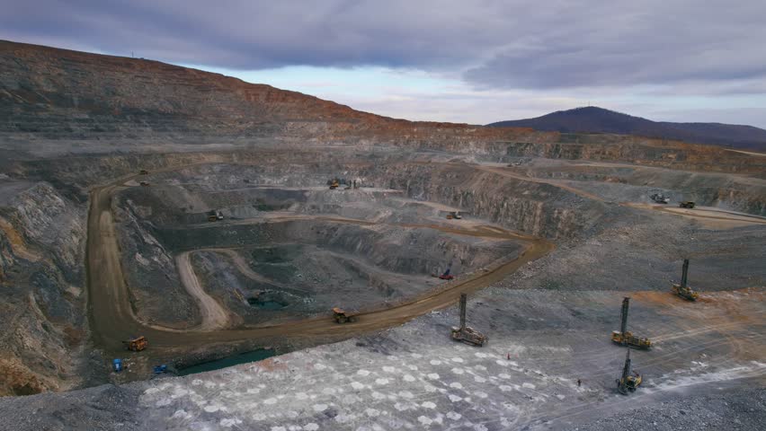 Drilling rigs drill holes to install explosives to blast rock mass in open pit mine. Aerial view Mining industry gold ore with big dump truck.