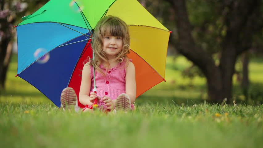 Girl with umbrella sitting on grass and smiling
