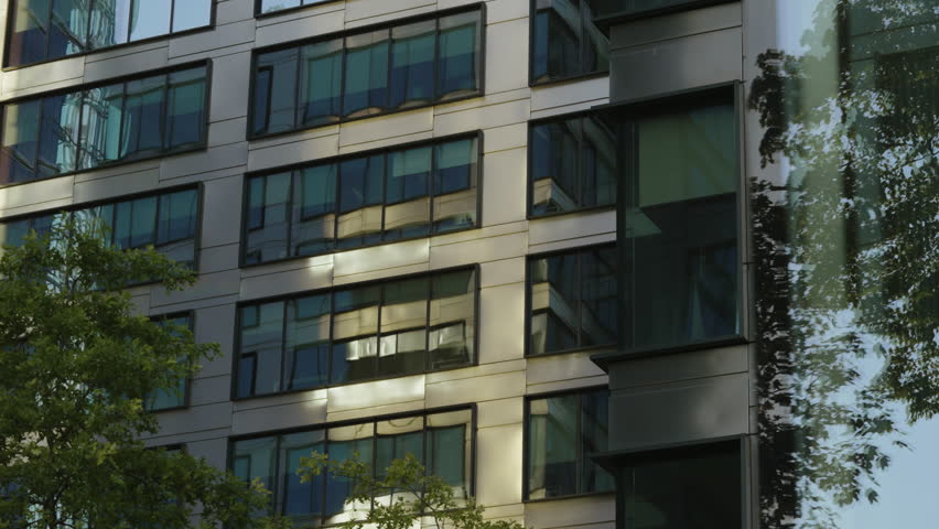 Close-up gimbal or dolly shot of modern skyscraper windows and blue sky mirrored in glass surface, summer day cityscape, high-rise buildings in motion, business district details