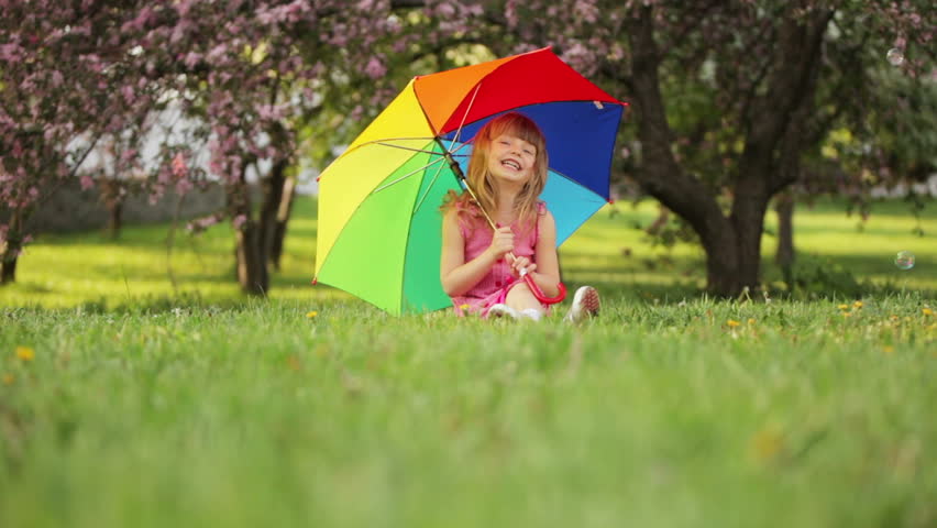 Child with umbrella sitting on grass and smiling

