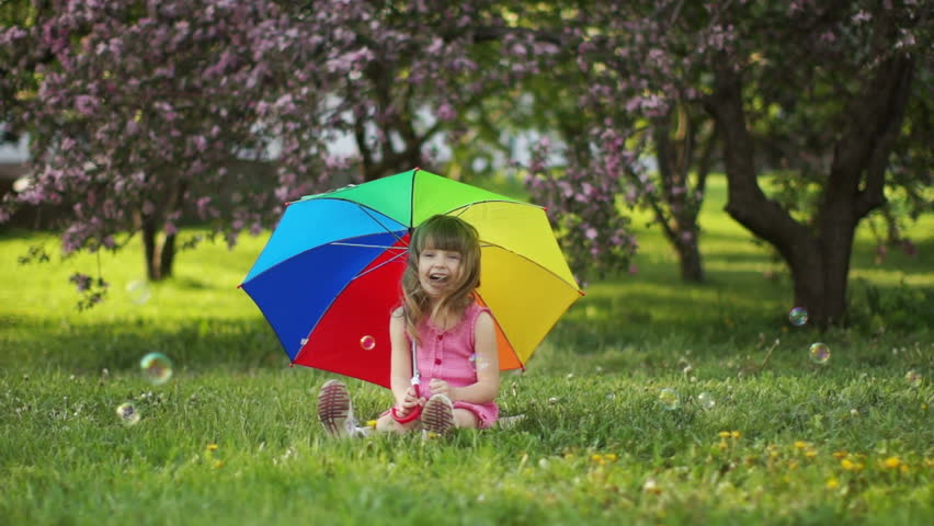Cute little girl sitting on grass with umbrella
