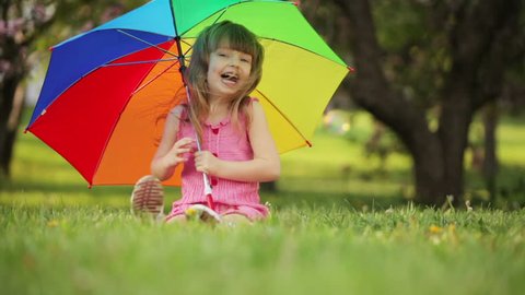 Cute girl with umbrella sitting on grass and laughing
