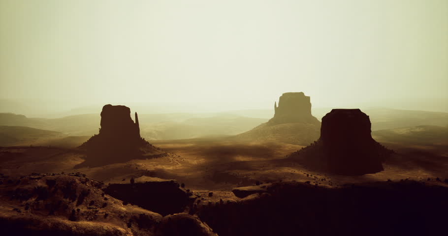 Various towering rock formations rise from a vast desert under a warm, golden light. The landscape stretches endlessly, creating a stunning view at dusk.
