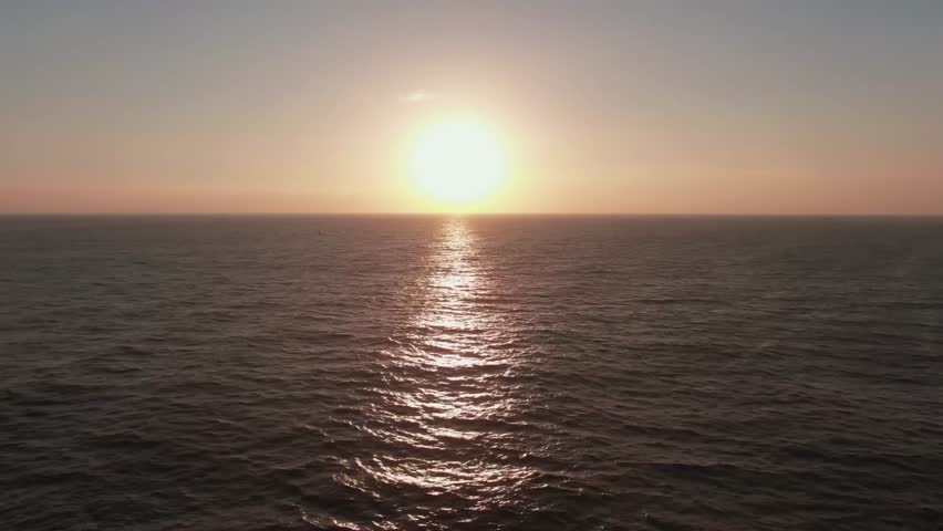 Aerial view of the glowing sun setting over the ocean horizon.
