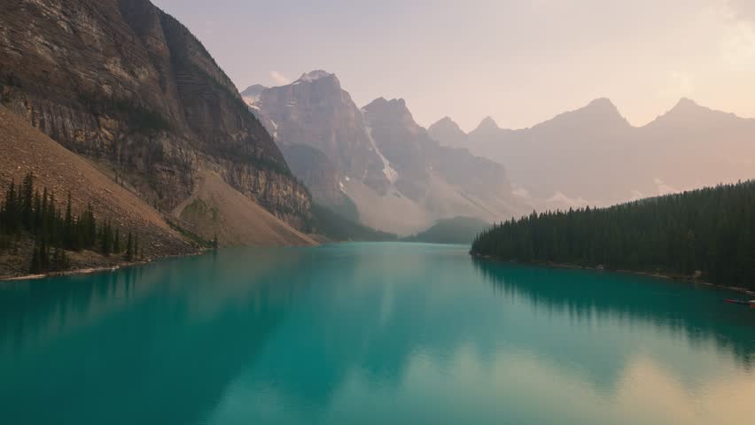 Moraine Lake in Banff National Park, Alberta, Canada, surrounded by towering mountains and lush trees. The turquoise water reflects the peaks under a soft, golden sunset sky.