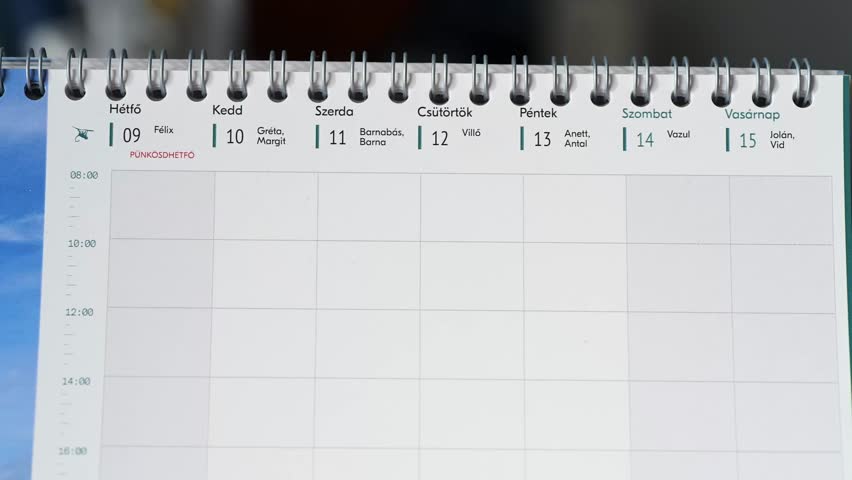 Close-up of a Hungarian weekly calendar showing the days from Monday to Saturday, with names associated with each date. A person is flipping the page, revealing part of the next week.