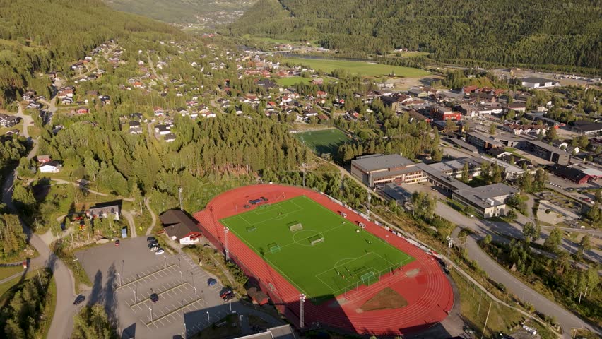 Aerial drone glide reveal of Gol Idrettsarena in Gol, Buskerud, Norway. Sports facility with fields, tracks, and surrounding landscape.
