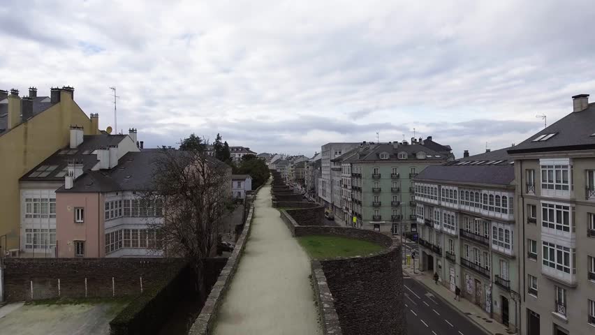 Aerial drone take-off over the adarve of Lugo’s Roman Wall at Porta de San Fernando. People strolling and vehicles passing nearby. UNESCO World Heritage Site, Galicia, Spain.