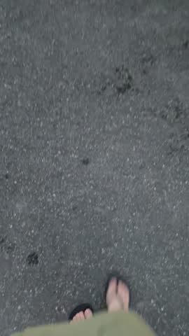 POV. Top view legs with flip flops shoes under army green skirt walking on asphalt road. First person point of view. Summer day walk concept. Dusk time.