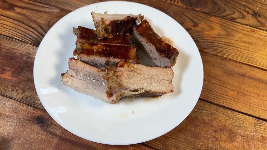 Sliced pork ribs, baked in special sauce lie on a white plate on a wooden rustic table, top view 
