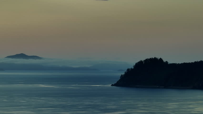 Aerial: Drone shot tracking past a forested silhouetted island with other partially clouded islands on the horizon. Whitsundays, Australia