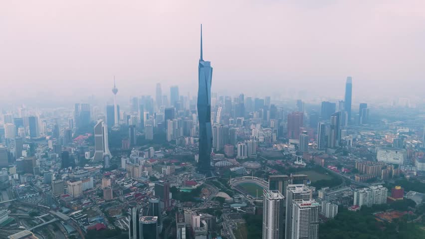 Aerial view of Kuala Lumpur cityscape under haze, featuring Merdeka 118, KL Tower, and surrounding skyscrapers. Captures urban density and air pollution over Malaysia’s capital.