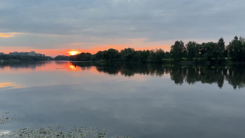 A quiet dawn in the city with gray clouds and a red sun over the river (4K60)