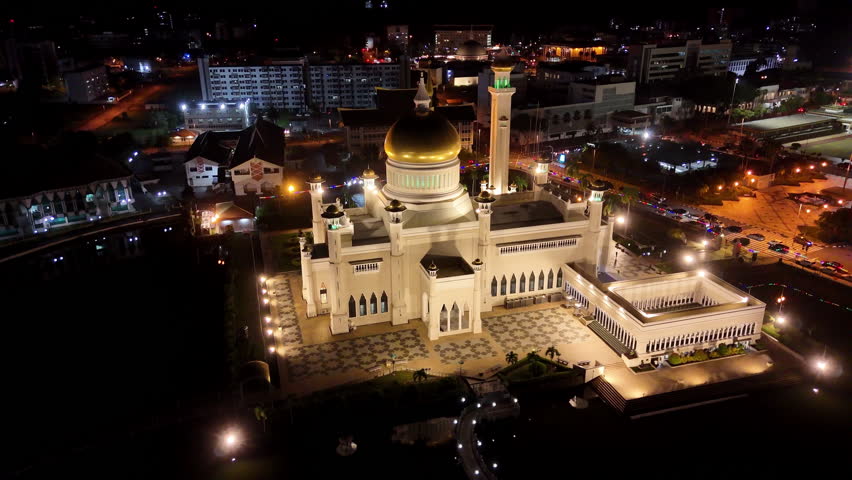 Epic cinematic aerial drone shot orbiting the Omar Ali Saifuddien Mosque lit up at night in Brunei.