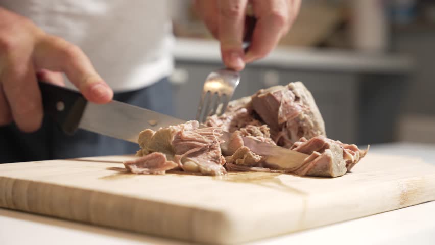Cutting tender meat. A person cuts soft, cooked meat on a wooden board using a knife and fork, revealing juicy, tender fibers. Perfect for cooking visuals