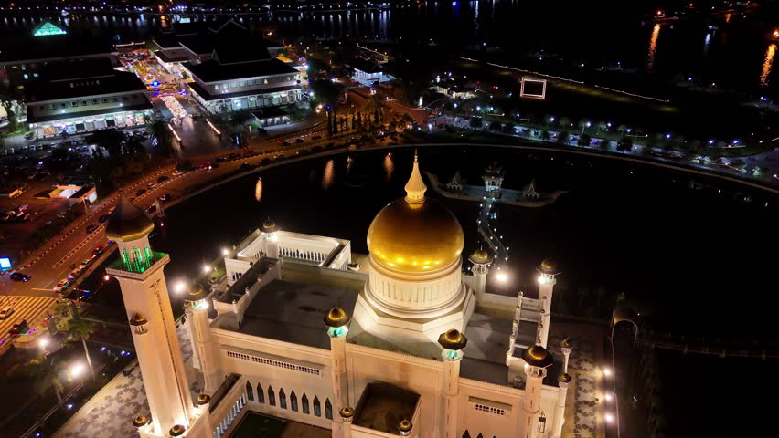 Epic cinematic rotating drone shot orbiting the lit up Omar Ali Saifuddien Mosque at night in Brunei.