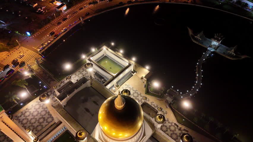 Epic cinematic aerial drone shot orbiting and showcasing the lit up Omar Ali Saifuddien Mosque at night in Brunei.