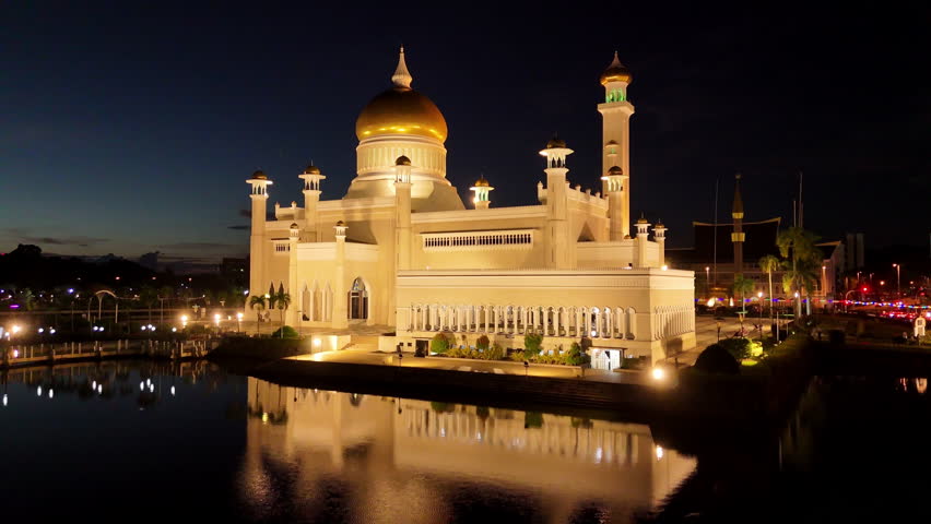 Epic cinematic aerial drone shot close up to the Omar Ali Saifuddien Mosque at night, being lit up by it's lights in Brunei.