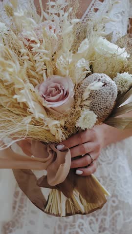 Bride holding wedding bouquet of roses, dried flowers and pampas grass, as well as dried wildflowers. Close-up of boho style wedding bouquet. Vertical video.