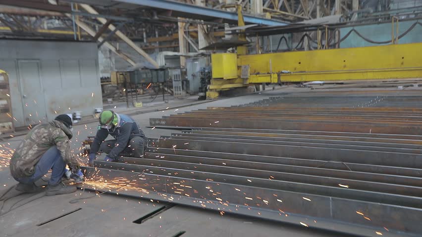 Worker Grinding Metal Plate. Steel structure metalworking shop. A worker grinds a metal plate or sheet with a hand grinder. Worker preparation steel plate by hand grinding machine.
