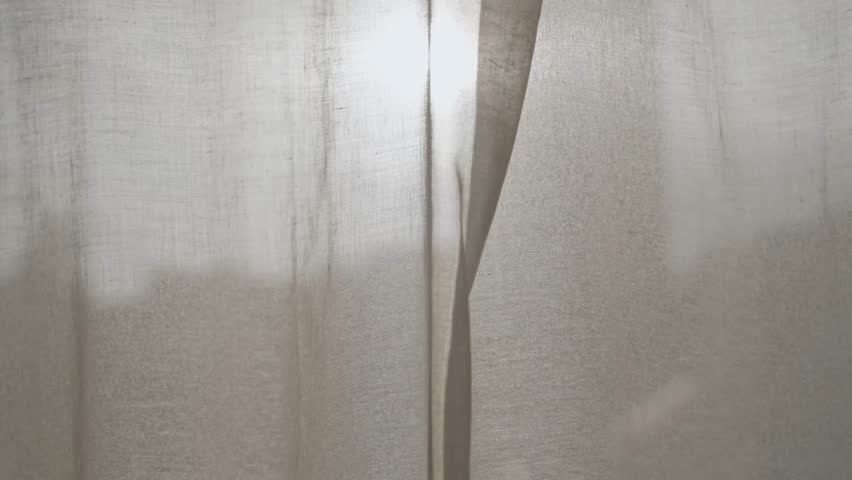 Male hand opens window curtain or drape to reveal sunset or sunrise outdoors. Man moves fabric to show the light of day outside in city or urban view. Warm sunlight shining in creating artistic flare