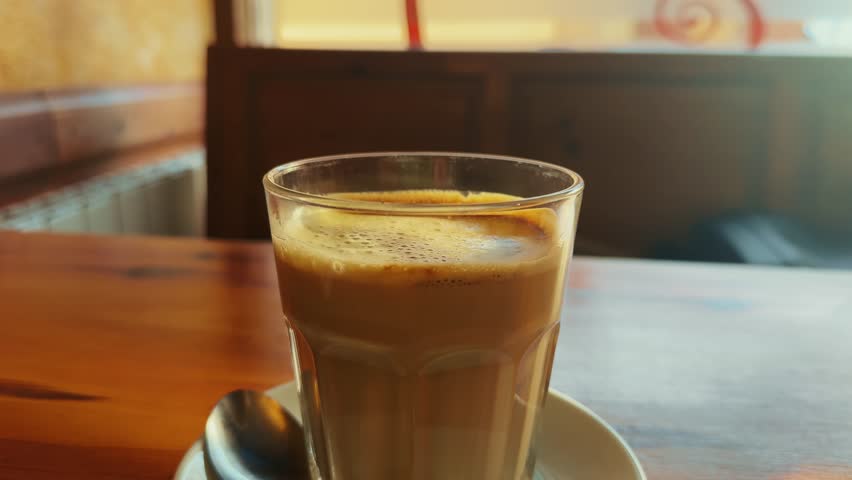 Transparent cup of coffee with milk on the wooden table at the light cozy cafe.