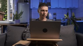 Man receives good news on laptop, celebrates and smiles, casual clothes, sitting on sofa in home kitchen, authentic real life moment. - Powered by Shutterstock - Get 15% off with code: PIKWIZARD15